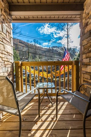 A wooden deck with a table and chairs, an American flag, and a view of trees and hills.