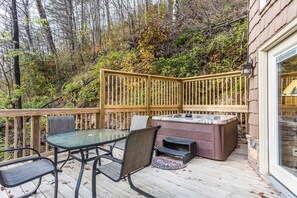 Una terraza con mesa y sillas de vidrio, un jacuzzi y un cerco de madera.