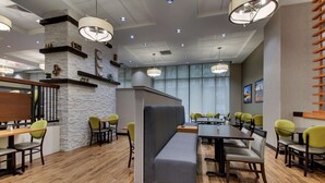 A modern restaurant with wooden flooring, green and yellow chairs, and a central seating area with a bench.