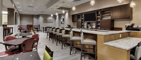 A modern hotel lobby with a bar area, seating arrangements, and a large screen.
