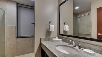 A modern bathroom with a granite countertop, a sink, a mirror, and a shower area.