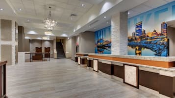 A spacious lobby with a modern reception desk, a staircase, and a cityscape mural on the wall.