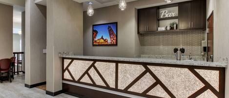 Un espace d’accueil d’hôtel au design moderne, comprenant un comptoir de réception, un tableau encadré représentant un bâtiment et une enseigne de bar.
