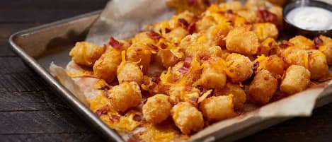 Eine Portion Tater Tots mit Käse und Speck, serviert auf einer Metalltablett mit einer Dipsoße.