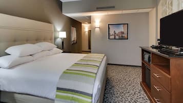 A hotel room with a large bed, a flat-screen TV, a wooden dresser, and a patterned carpet.