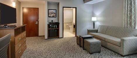 A hotel room with a sofa, a TV, a desk with drawers, a microwave, and a bathroom visible through an open door.