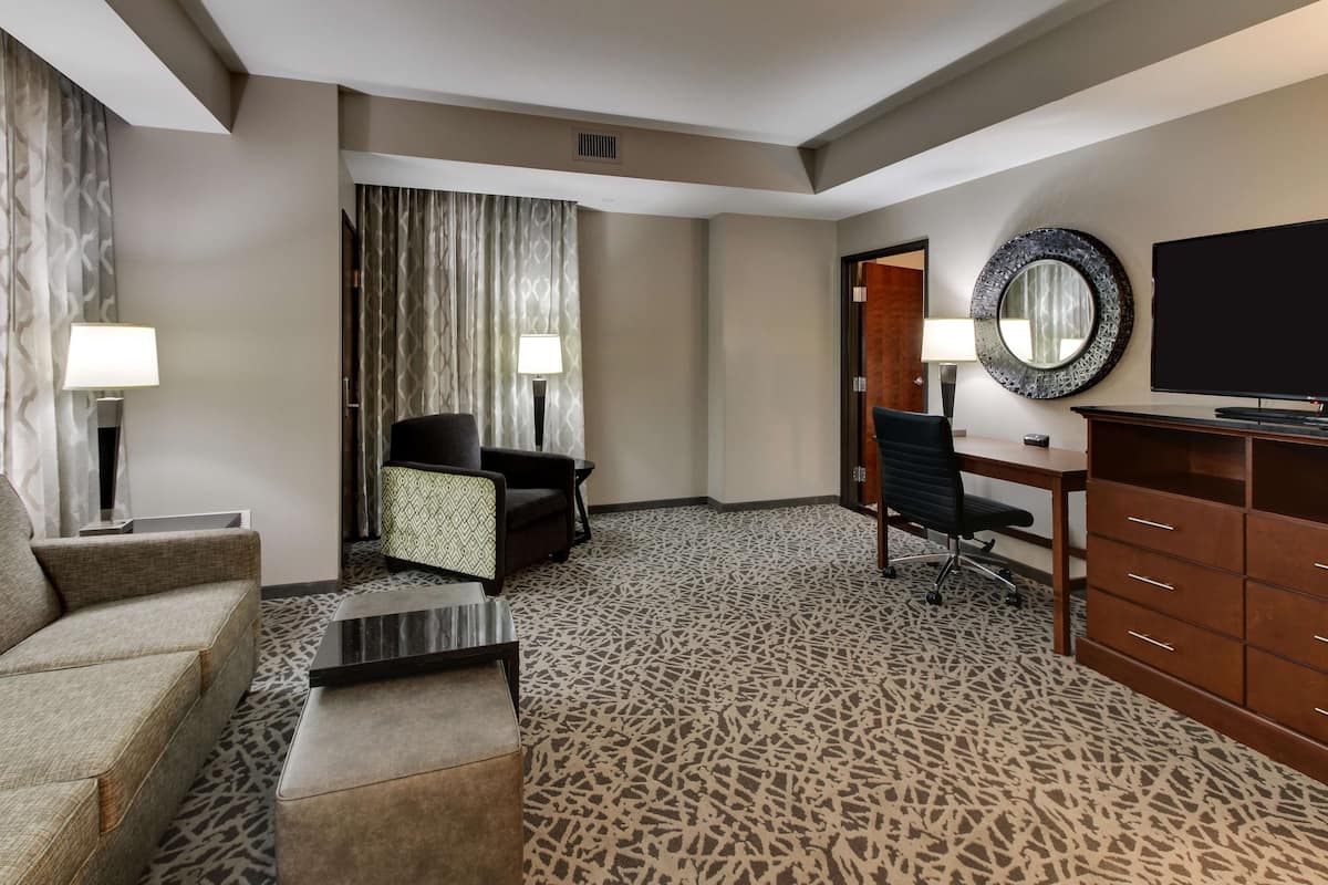 A hotel room with a sofa, two armchairs, a coffee table, a TV, a desk, and a dresser.