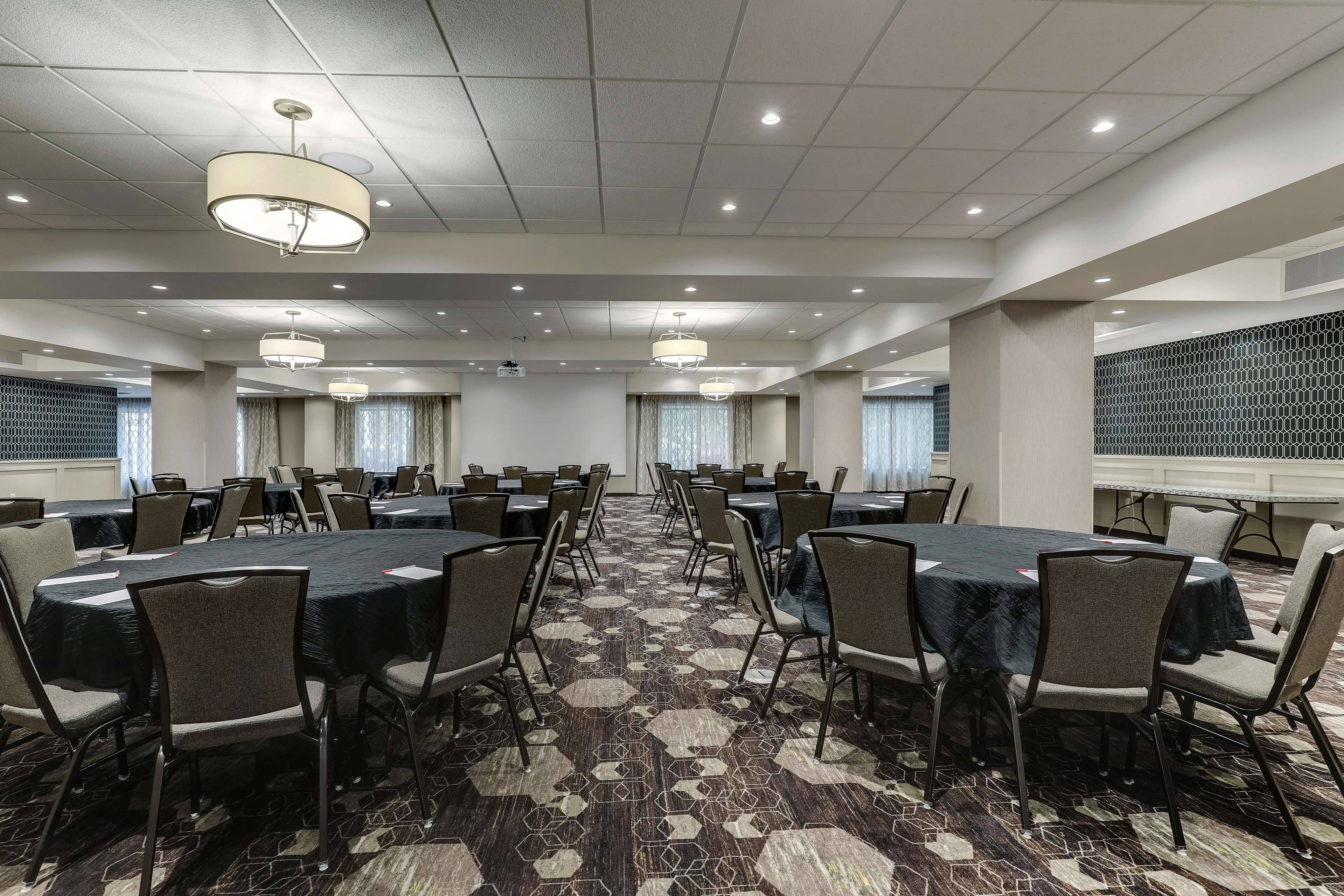 A conference room with multiple tables and chairs, a patterned carpet, and ceiling lights.