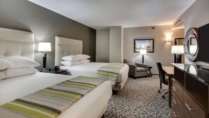 A hotel room with two beds, a desk, a chair, a dresser, and a television.