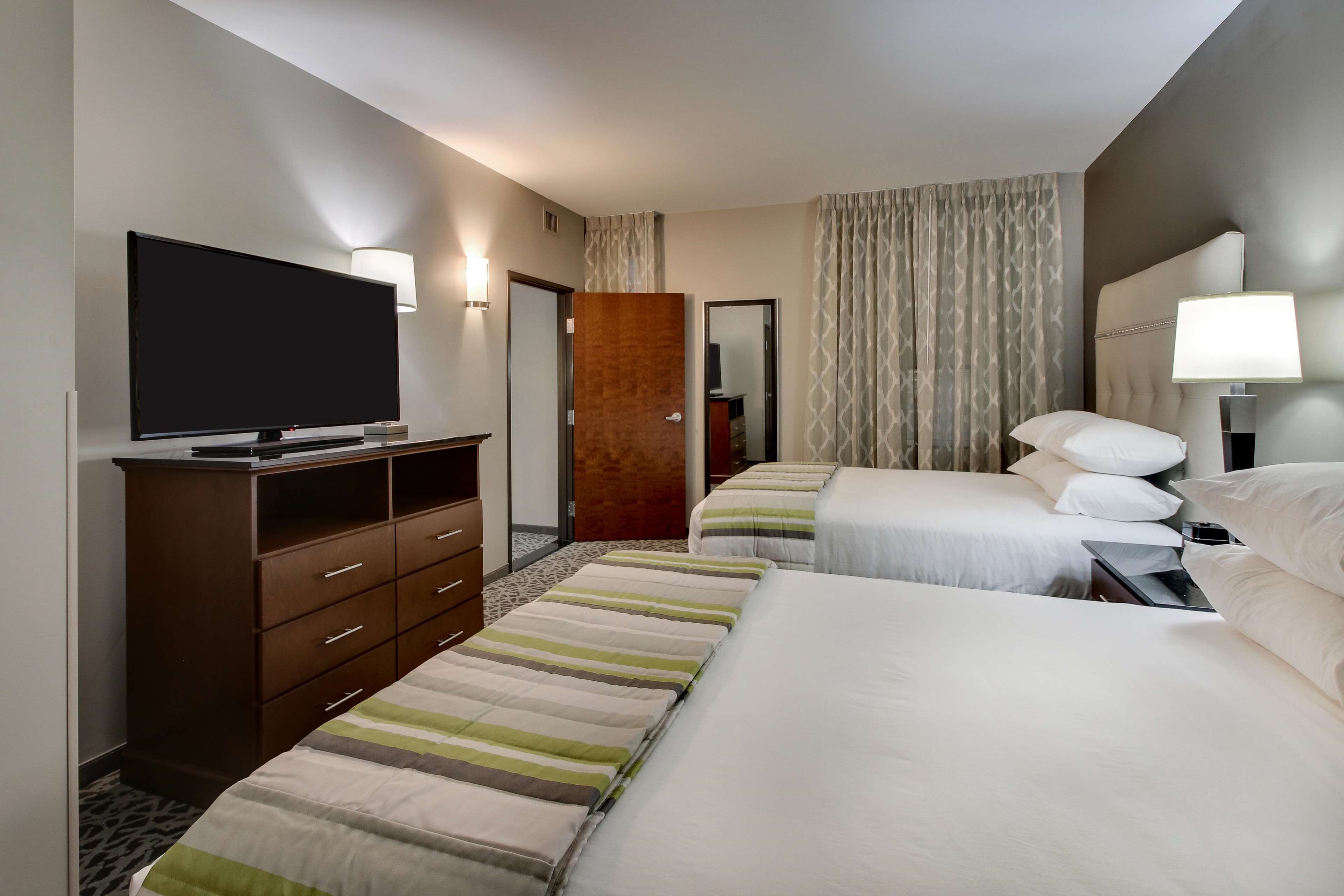 Ein Hotelzimmer mit zwei Betten, einem Fernseher, einem Schminktisch und einem Spiegel.
