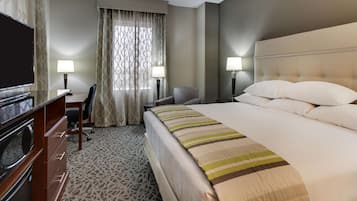 Una habitación de hotel con una cama, un escritorio, una silla, un televisor y dos lámparas.