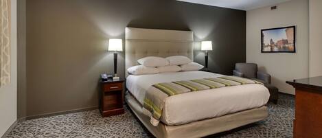 A hotel room with a large bed, two bedside lamps, a chair, a desk, and a framed picture on the wall.