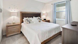 A bedroom with a large bed, two bedside tables, a desk, and a window with curtains.