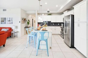 A modern kitchen with white cabinets, a stainless steel refrigerator, and a dining area with blue chairs.