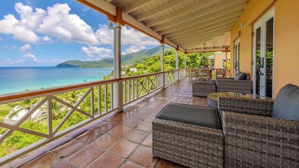 Ein überdachter Balkon mit Korbmöbeln, Blick auf den Ozean und eine gebirgige Landschaft.
