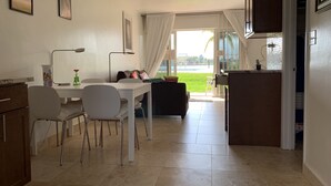 Cocina moderna con comedor, sofá y vista a un paisaje verde a través del ventanal.