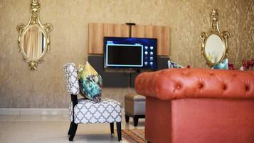 Een woonkamer met een televisie, twee sierlijke spiegels, een gestreept fauteuil en een rode poef.