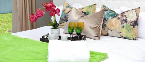 Una cama bien hecha con una toalla verde, un albornoz blanco y una bandeja con dos vasos y una planta.