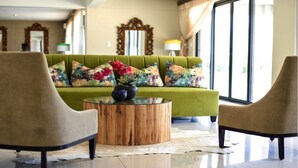 A living room with a green sofa, two armchairs, a wooden coffee table, and a vase with flowers.