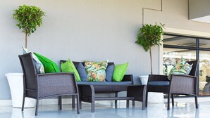 A modern outdoor seating area with wicker furniture and green cushions, two potted plants, and a glass wall.
