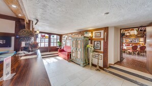 Eine Hotellobby mit einem Holzbüro, einem roten Sofa, einem alten Schrank und einem Essbereich mit Holztischen und Stühlen.