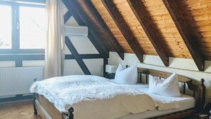 Ein Schlafzimmer mit Holzboden, einem Bett mit weißer Bettwäsche, einem Nachttisch und einem Fenster mit Vorhängen.