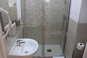 Un baño con ducha envuelta en vidrio, un lavamanos con grifo cromado y un dispensador de papel higiénico en la pared.