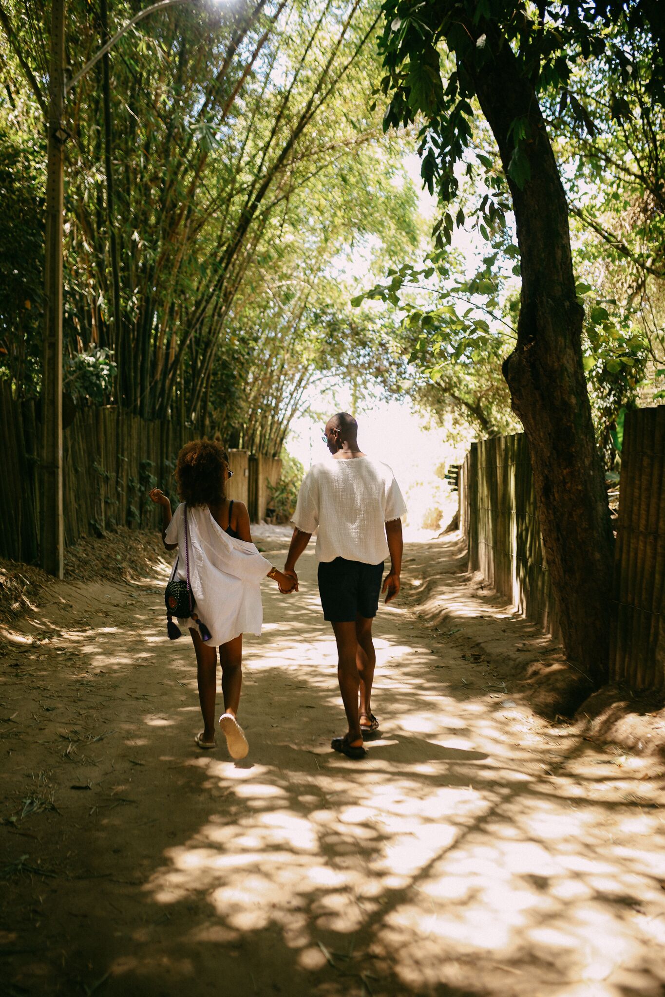 A couple walking down a dirt path lined with bamboo and trees.