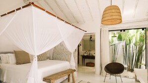 A bedroom with a canopy bed, a wooden bench, a chair, and a view of a bathroom and plants. - Casa La Torre - Hotel Boutique (Porto Seguro)