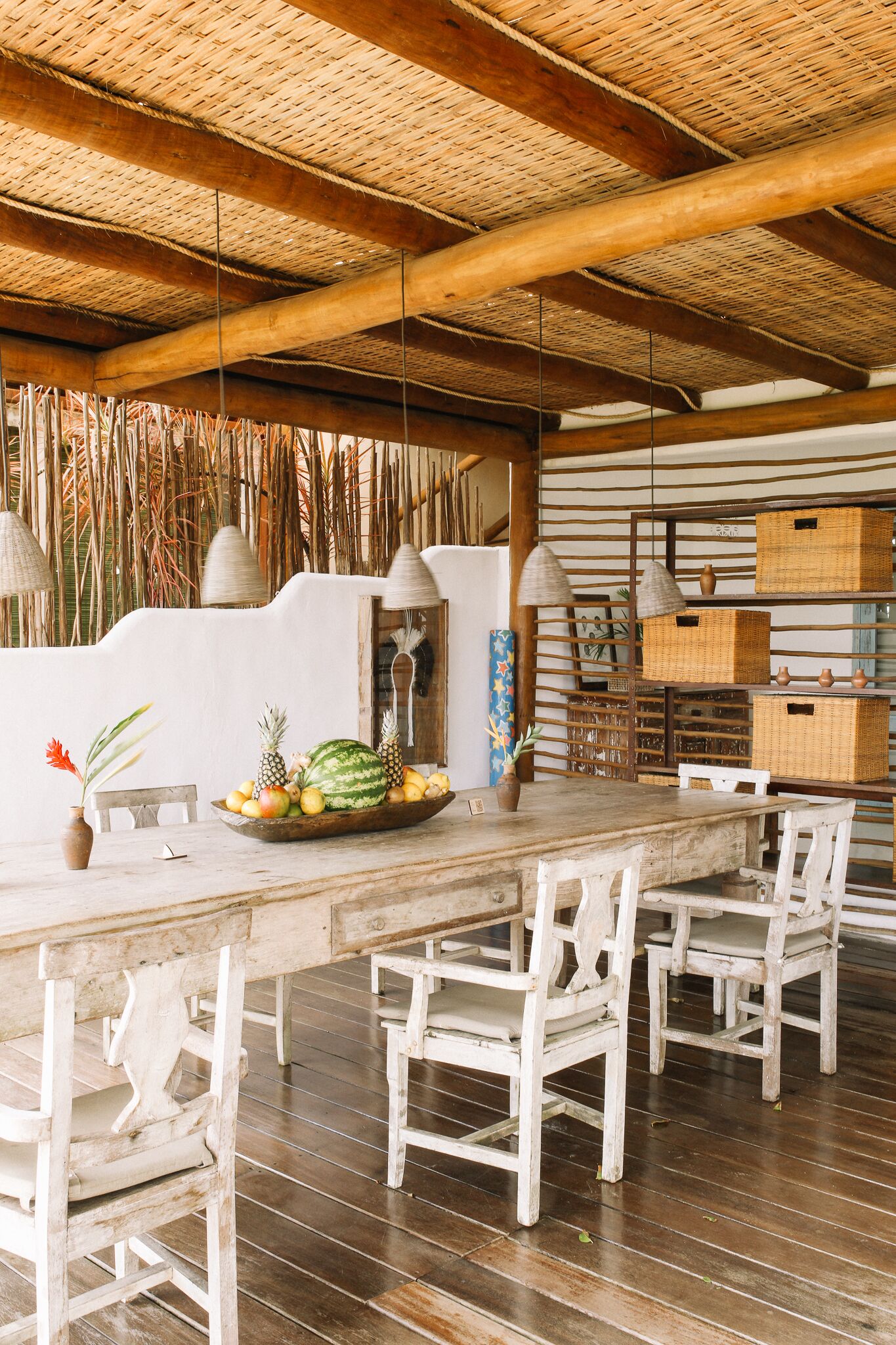 A rustic dining area with a wooden table, white chairs, and a woven ceiling.