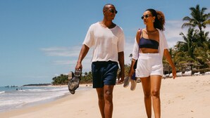 A couple walking on a sandy beach with palm trees and the ocean in the background. - Casa La Torre - Hotel Boutique (Porto Seguro)