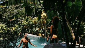 A pool area surrounded by lush tropical foliage, with a wooden deck and a stone wall. - Casa La Torre - Hotel Boutique (Porto Seguro)