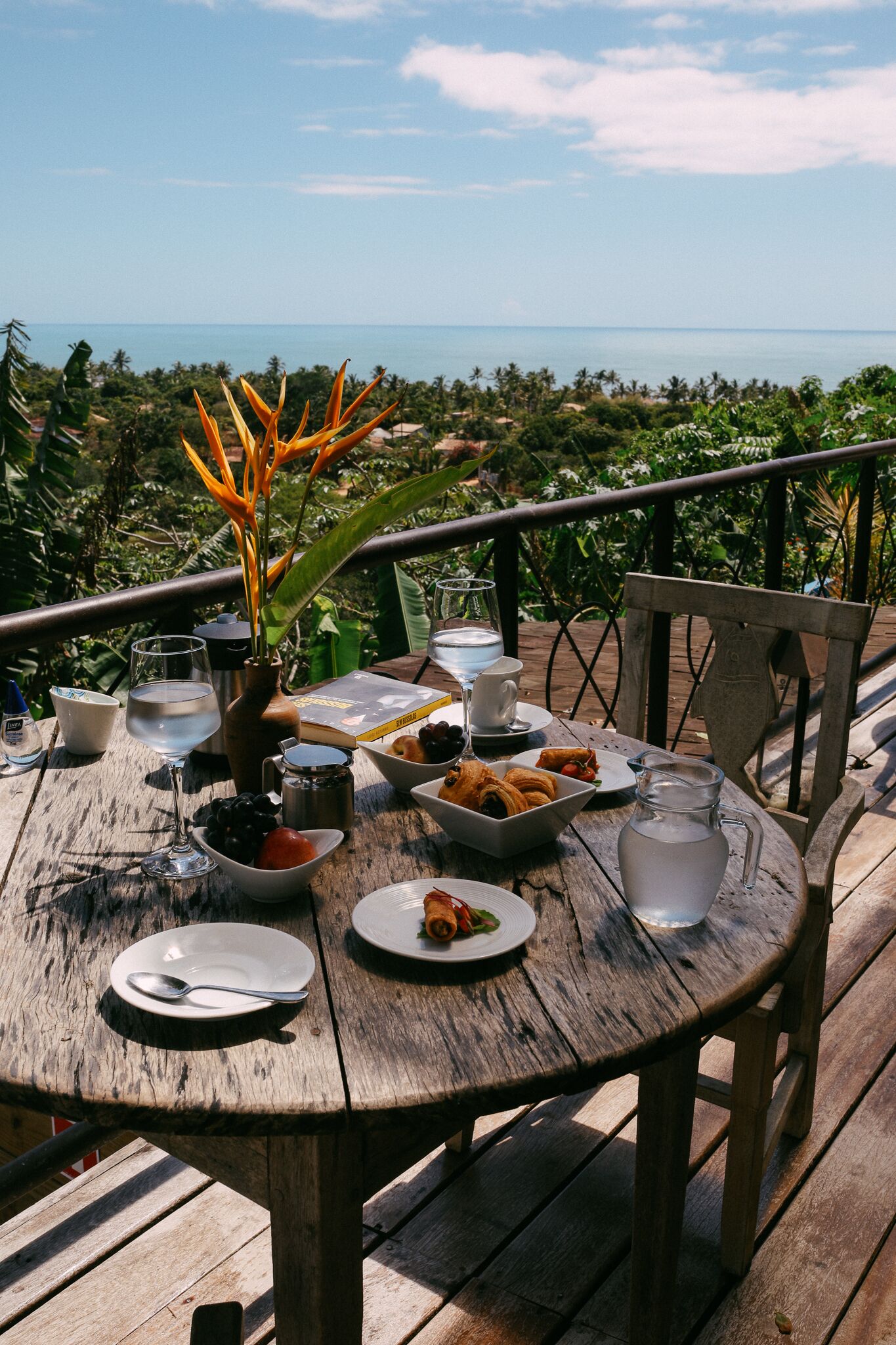 A wooden table with a view of the ocean, surrounded by greenery.