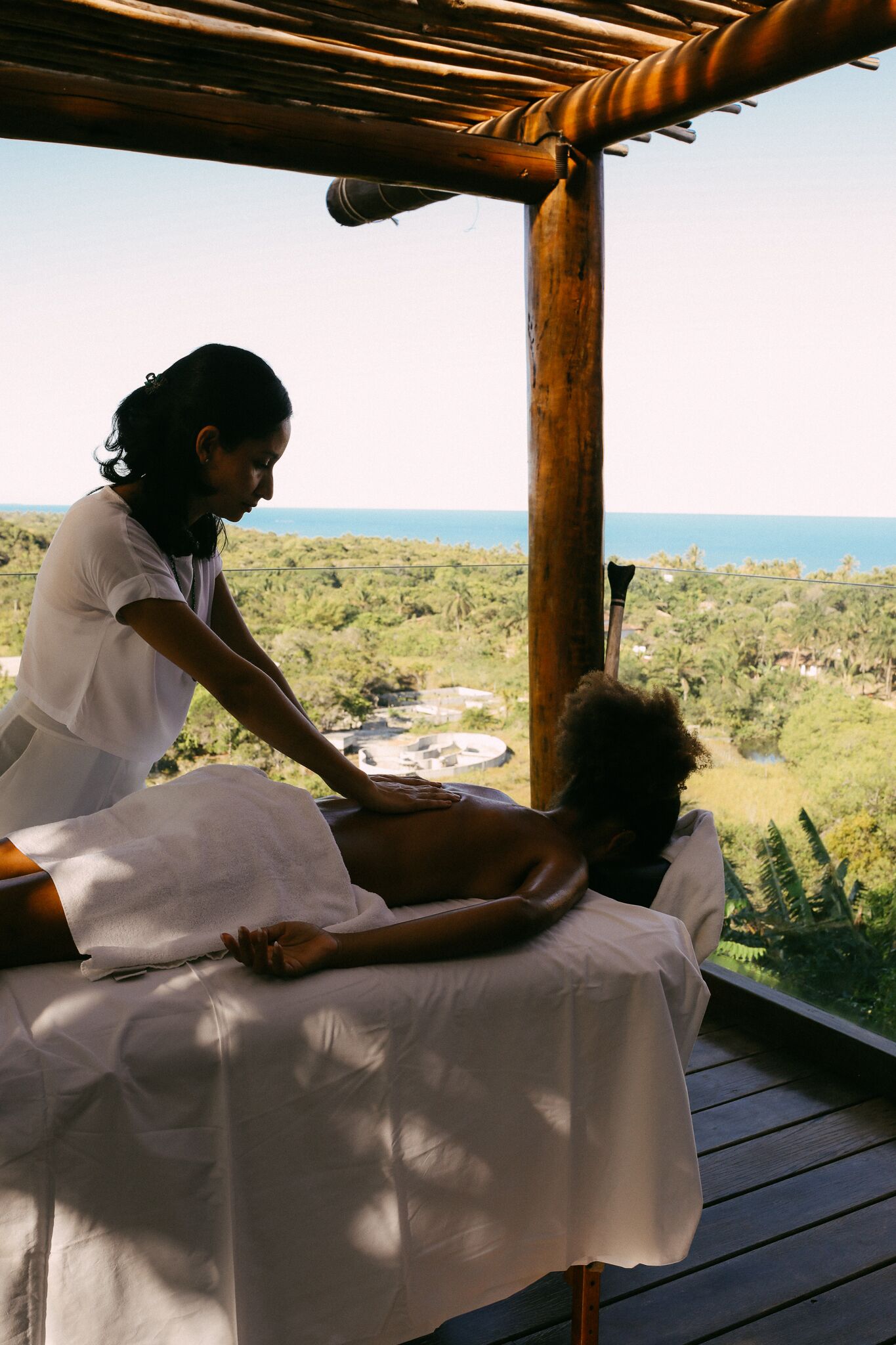 A massage therapy session on a wooden deck with a view of a lush landscape and the ocean.