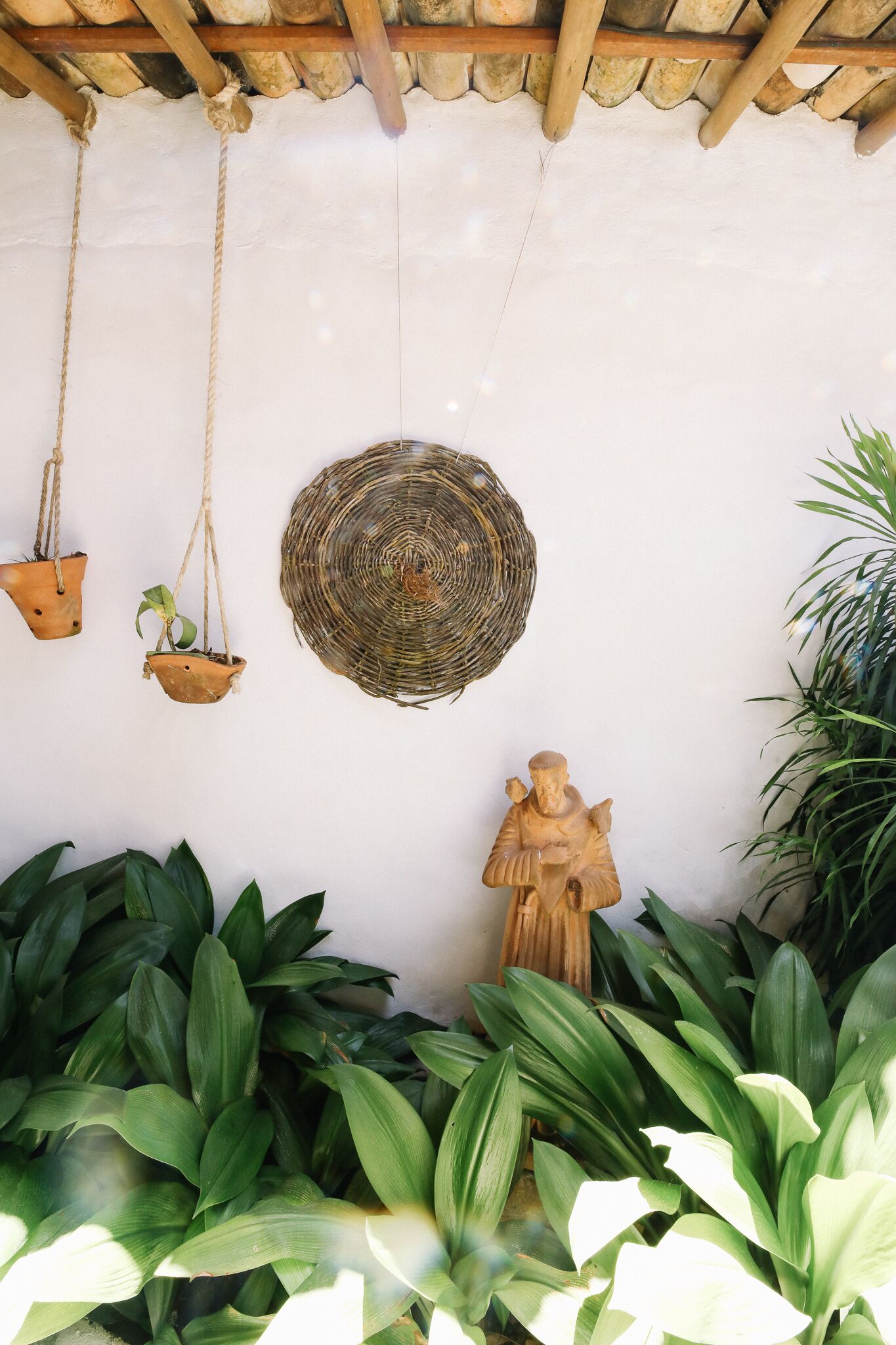A wall with hanging planters, a woven basket, and a statue.