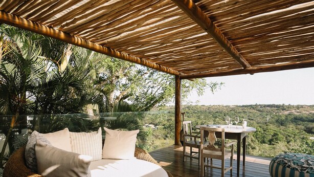 A wooden deck with a round wicker bed and a table with chairs, overlooking a lush landscape. - Casa La Torre - Hotel Boutique (Porto Seguro)