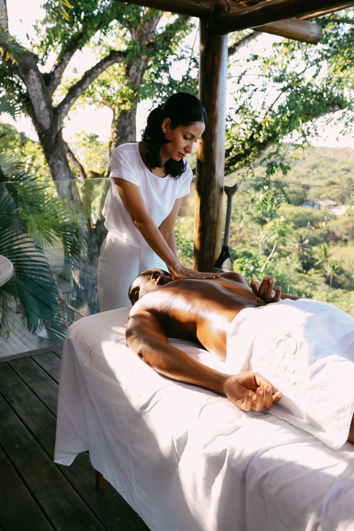 A person receiving a massage on a wooden deck with a view of a lush landscape.