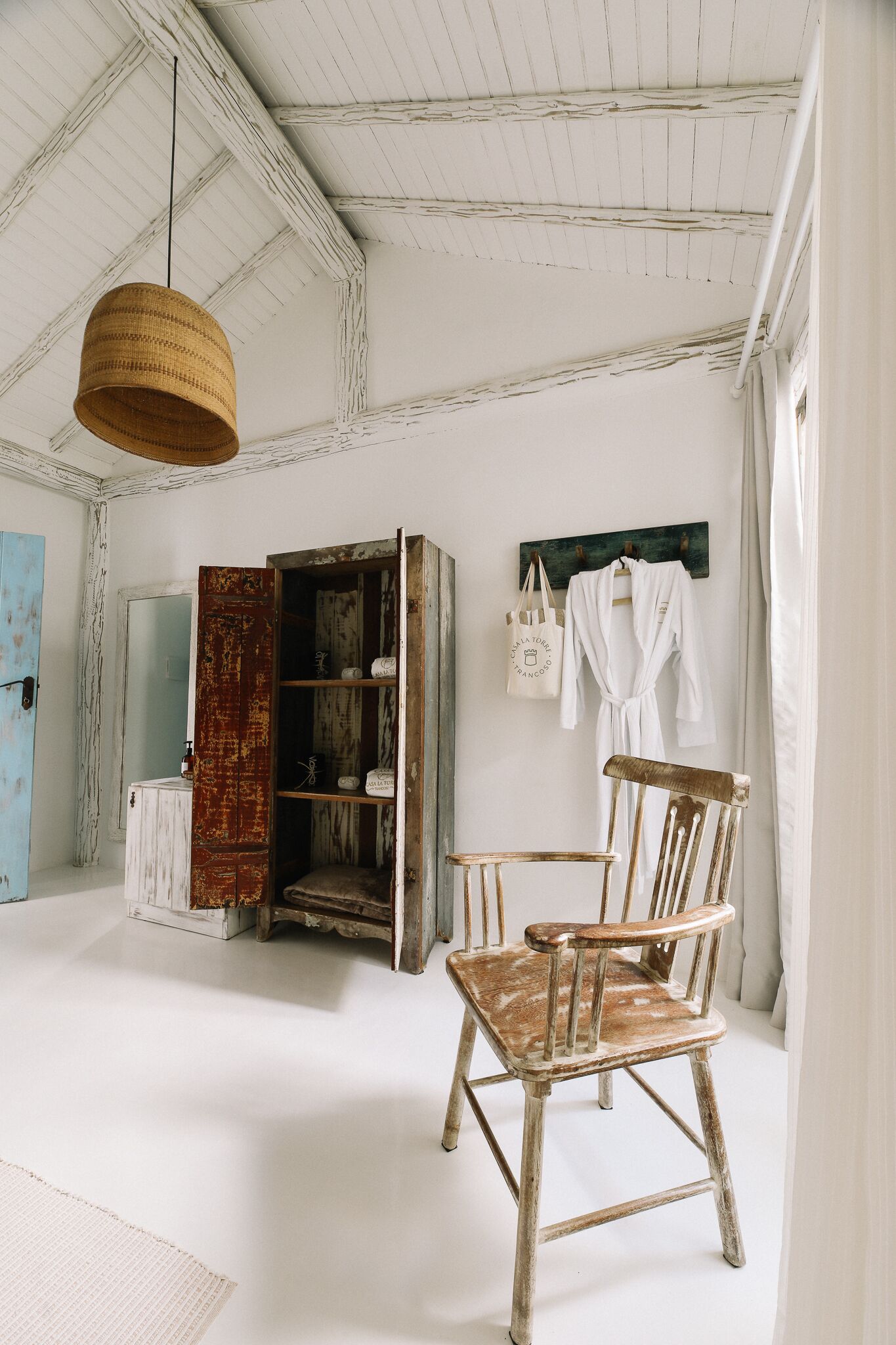 A rustic bathroom with a wooden chair, a hanging basket, and a shelf with toiletries.