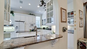 A spacious kitchen with white cabinetry, a granite countertop, and a stainless steel sink.