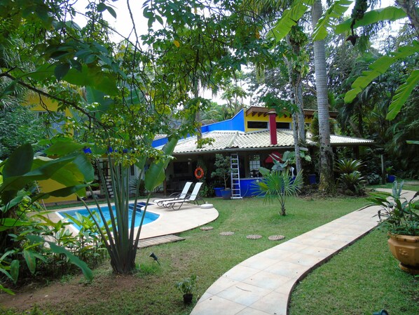 Una casa con piscina, rodeada de abundante vegetación y un césped cuidado.