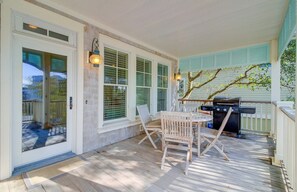 A covered porch with a grill, two chairs, and a table.