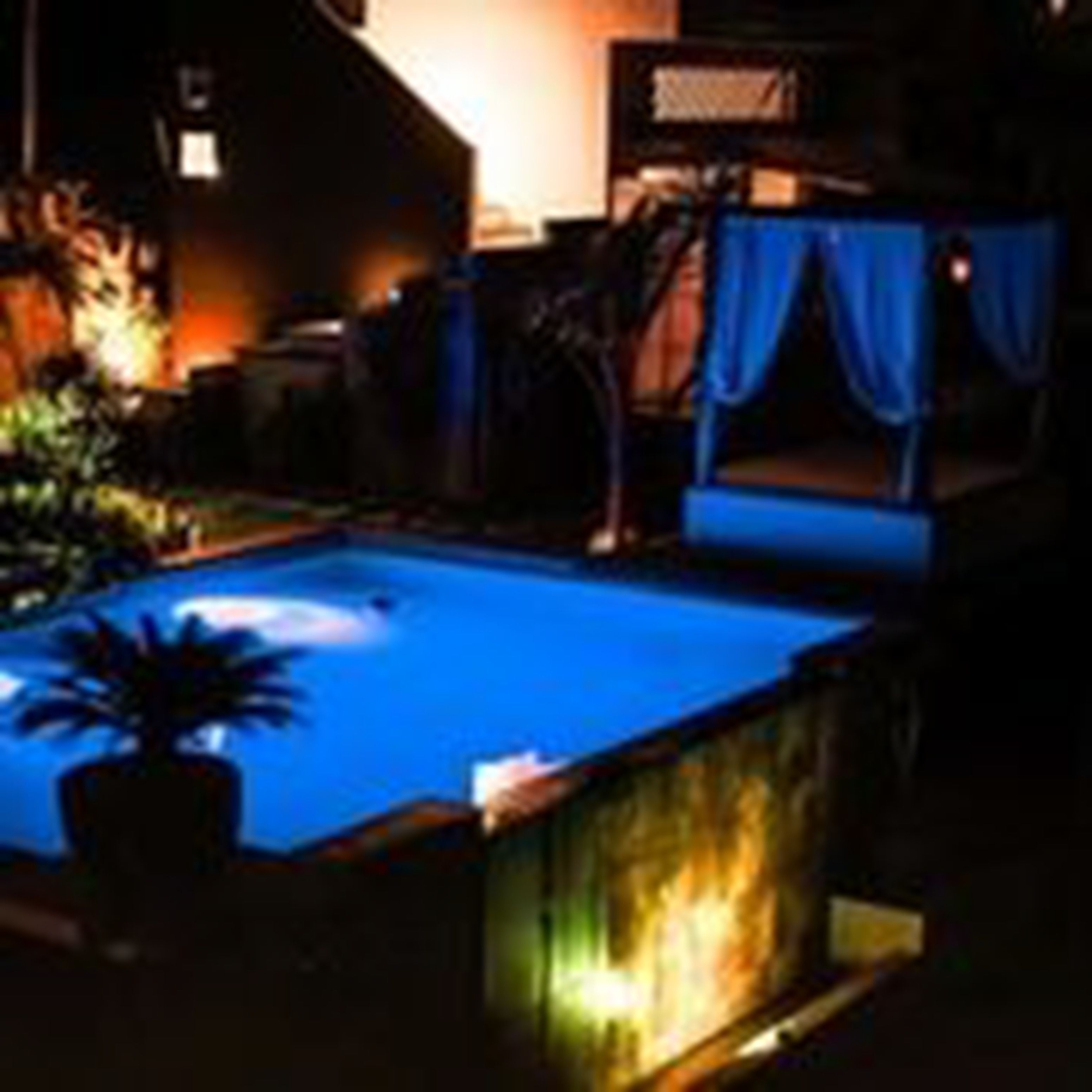 Piscina com elemento aquático azul, cercada por uma grade escura e um vaso de planta.