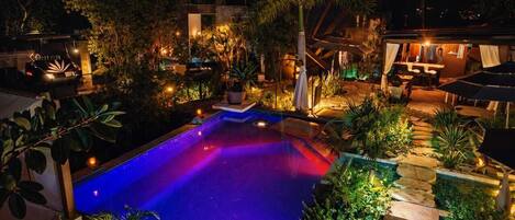 Vue nocturne d’un espace piscine, avec la végétation environnante et un bâtiment doté d’une terrasse.