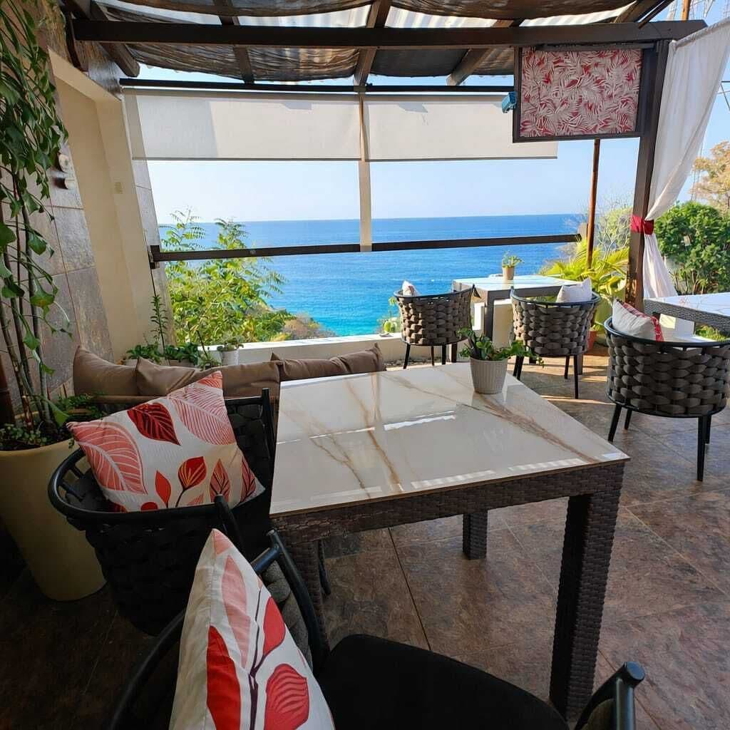 An outdoor seating area with a table and chairs, a view of the ocean, and potted plants.