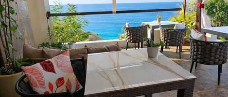 An outdoor seating area with a table and chairs, a view of the ocean, and potted plants.