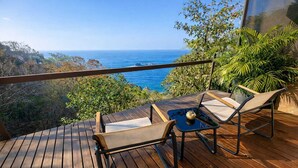 A wooden deck with two lounge chairs and a small table, overlooking a coastal landscape. - Casa Qi Mazunte (Santa María Tonameca)
