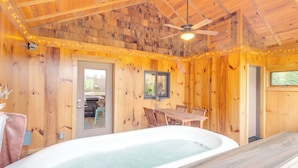 A wooden cabin interior with a hot tub, wooden walls, a dining table, and a ceiling fan.