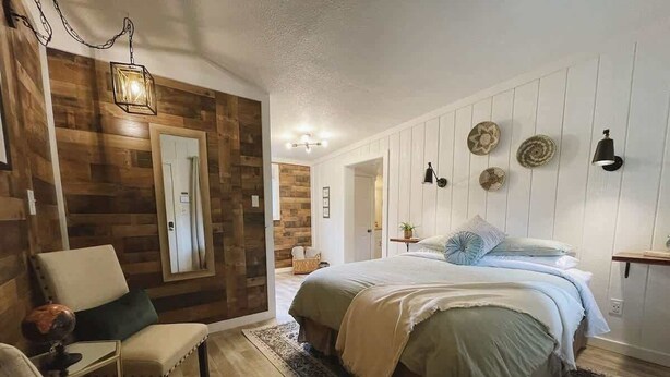 Ein Schlafzimmer mit einem Bett, zwei Stühlen, einem Teppich, Holzvertäfelung und Wandleuchten.