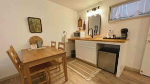 Eine kleine Küche mit Holztisch und -stühlen, einer Mikrowelle, einer Kaffeemaschine und einem kleinen Kühlschrank.