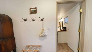 Ein Zimmer mit einer hölzernen Bank, einem Kleiderständer mit einer Tasche und einer Tür zu einem Badezimmer mit Spiegel und Waschbecken.